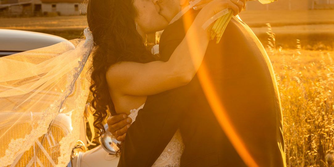 Novios abrazados con coche histórico a la puesta del sol